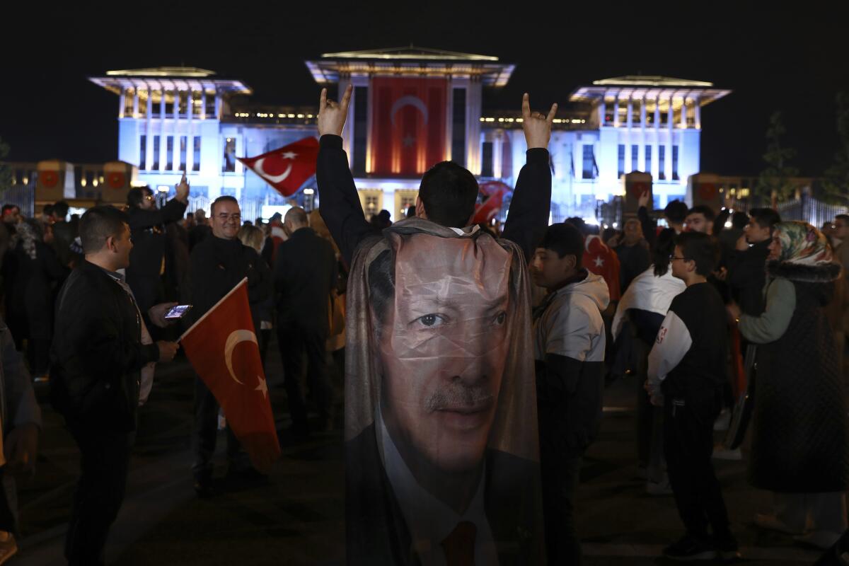 A man wearing a cape with President Recep Tayyip Erdogan's face stands with crowds in Turkey.
