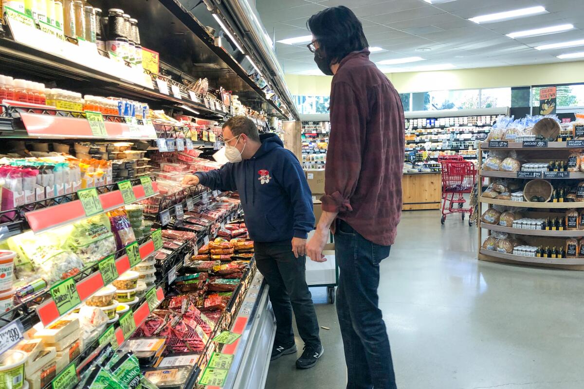 Two people look at items in a refrigerated aisle in a market.