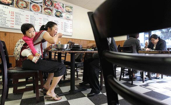 Su Yang, of Chino Hills, carries her 10-month-old daughter, Madelyn Seo, on her back while dining at Gamja-Gol, a restaurant in Los Angeles' Koreatown neighborhood.