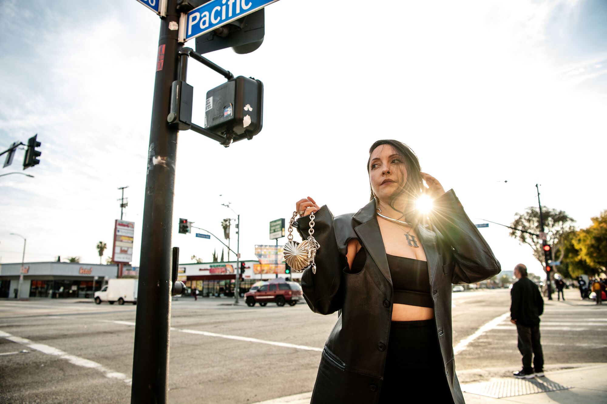 A woman stands at a corner beneath a street sign.