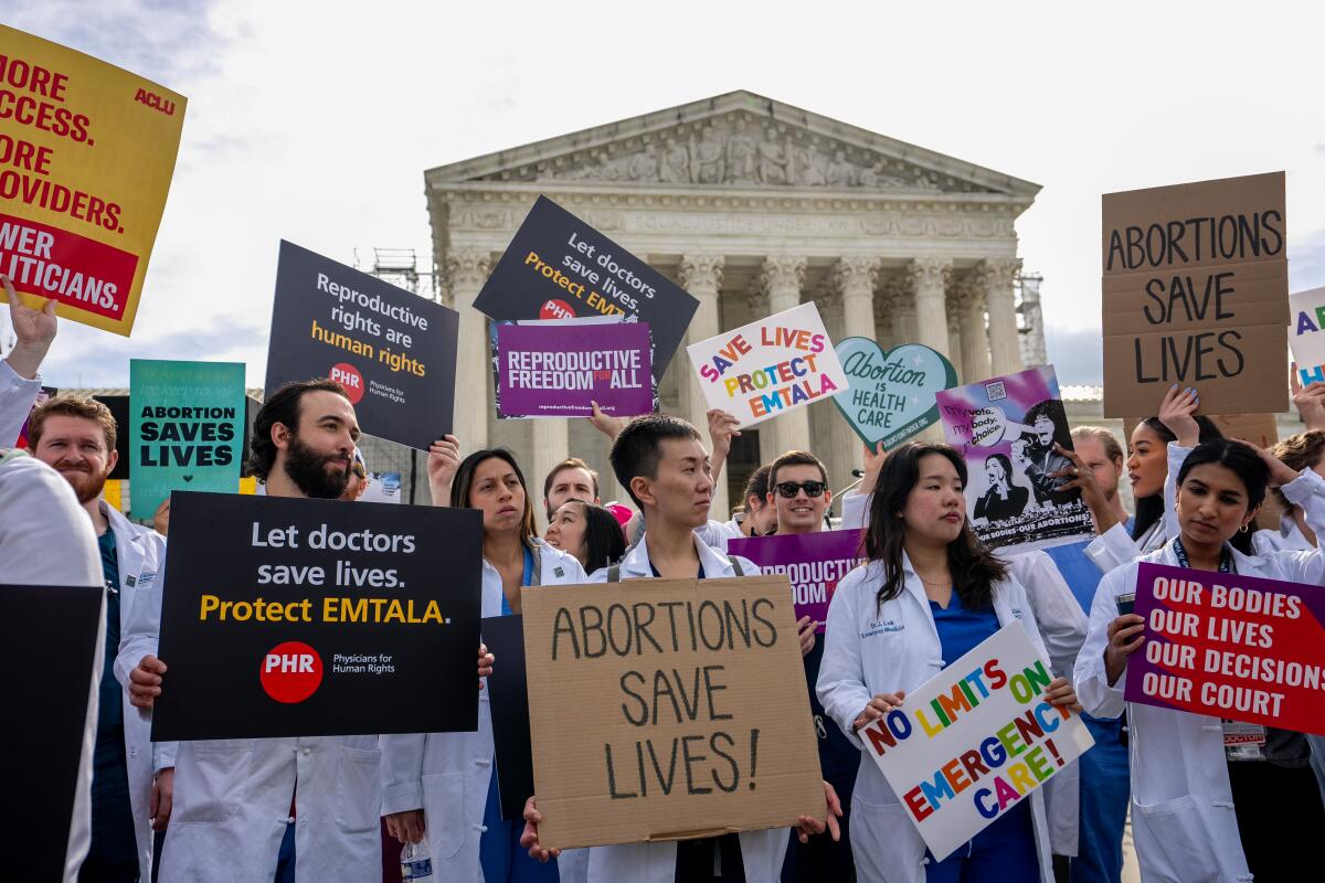 People in lab coats hold signs including "Abortions save lives" and "No limits on emergency care."