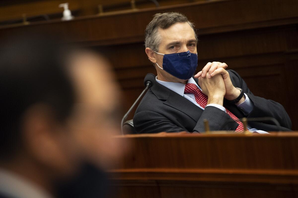 Man sits at a podium while wearing a mask