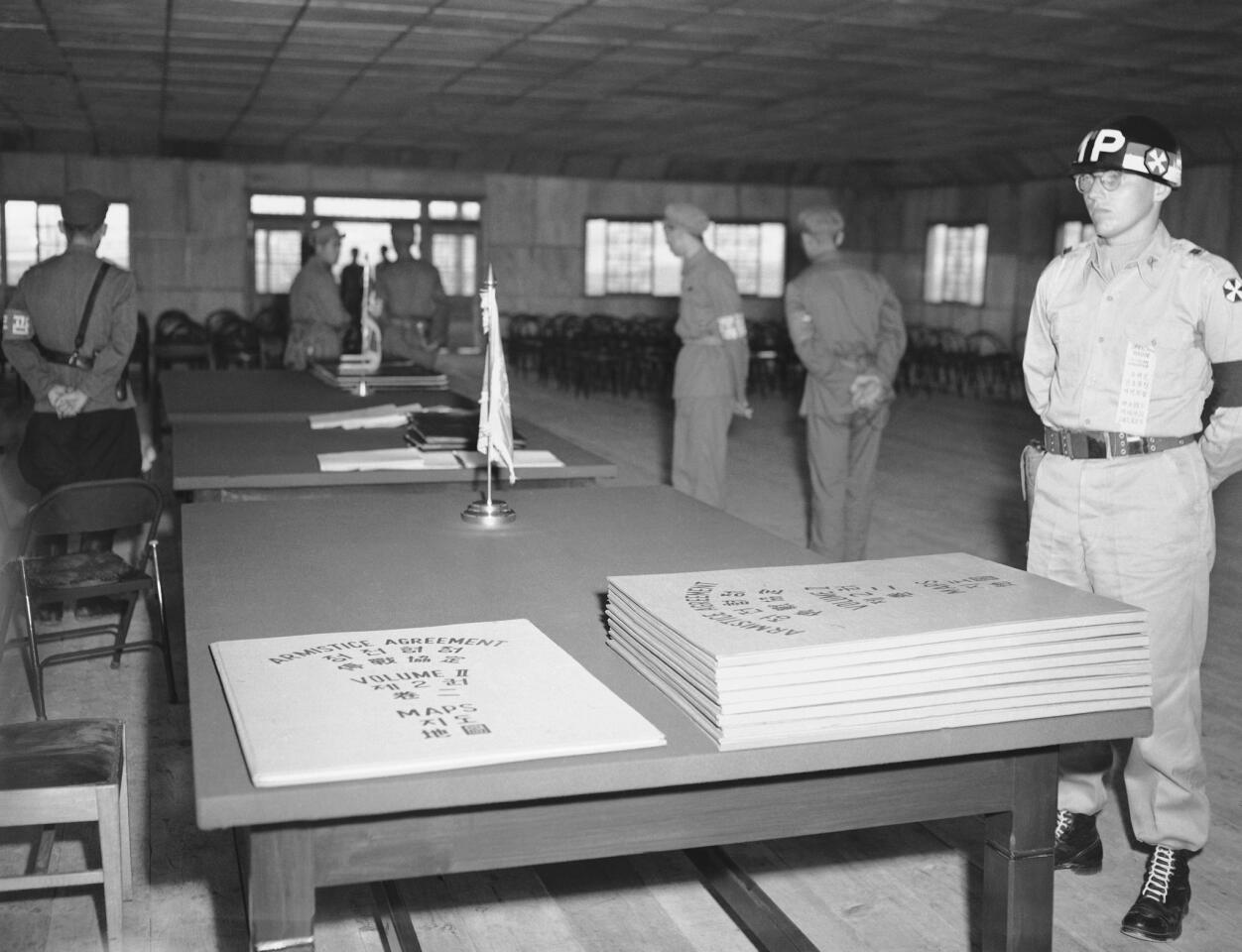 Lt. Martin H. Petersen of Franklin Park, N.Y., an MP on special detail, stands guard over the still-secret armistice documents as they lie on a table inside the armistice building at Panmunjom waiting to be signed by U.N. and Communist delegates. In background are North Korean security guards.