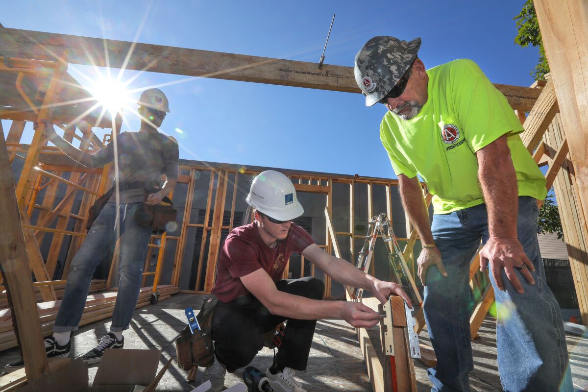 At the Warrior Village construction site at San Marcos High School, project instructor Alan Jurgensen of Associated General Contractors (right) gives advice to San Marcos High students Nick Przesmicki (center) and Cole Bradley as they work on a roof truss.