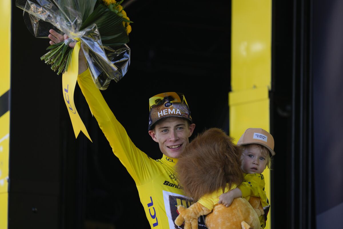 Jonas Vingegaard holds his daughter Frida as he holds up flowers on the podium.