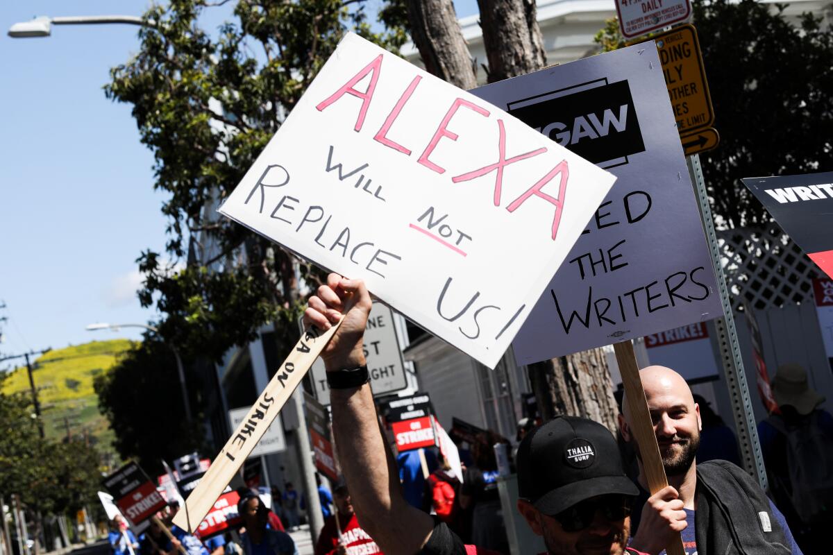 A striker walks a picket line holding a sign that reads, "Alexa will not replace us!"