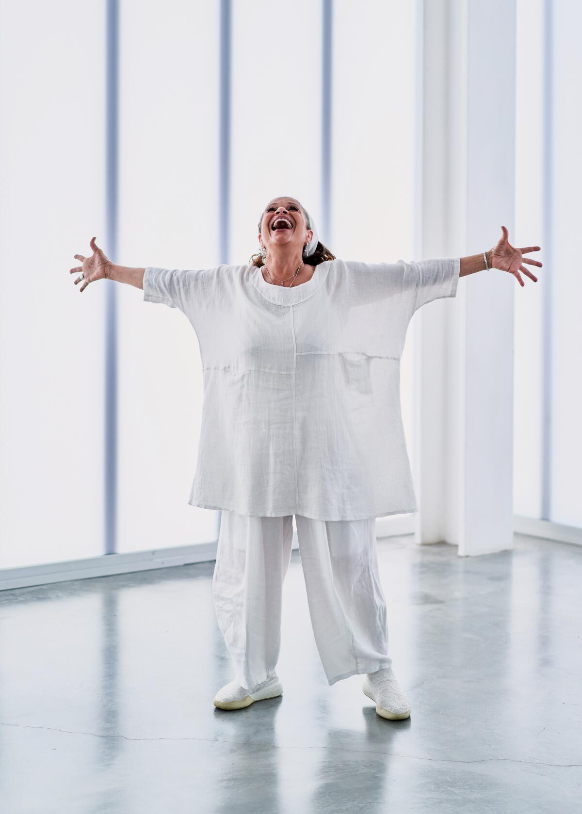 A woman wearing white reaches out her arms to her side in an expression of joy.