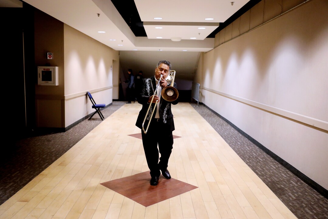 A musician warming up his trombone walks straight toward the camera 