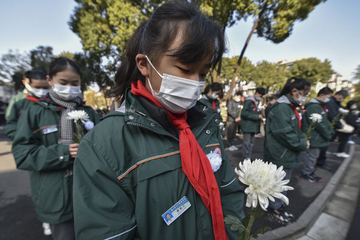 Students wearing face masks hold flowers mourn for the victims of the Nakjing Massacre at a mass burial site during the annual commemoration of the 1937 Nanking Massacre in Nanjing in eastern China's Jiangsu province, Monday, Dec. 13, 2021. China on Monday marking the 84th anniversary of the Nanking Massacre, in which it says hundreds of thousands of civilians and disarmed soldiers were killed by Japanese soldiers in and around the former Chinese capital. (Chinatopix Via AP)