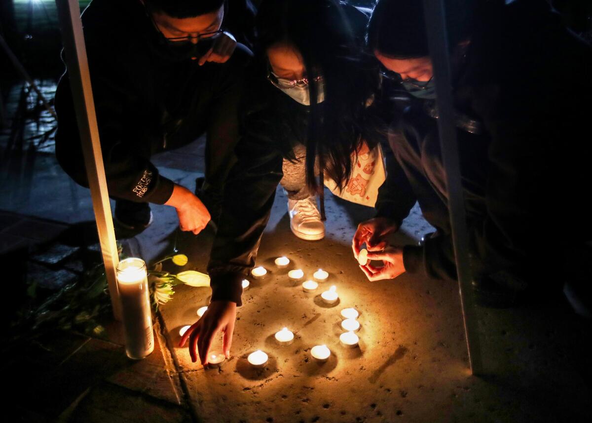 Three people squat to light tea candles in a shape of a heart.