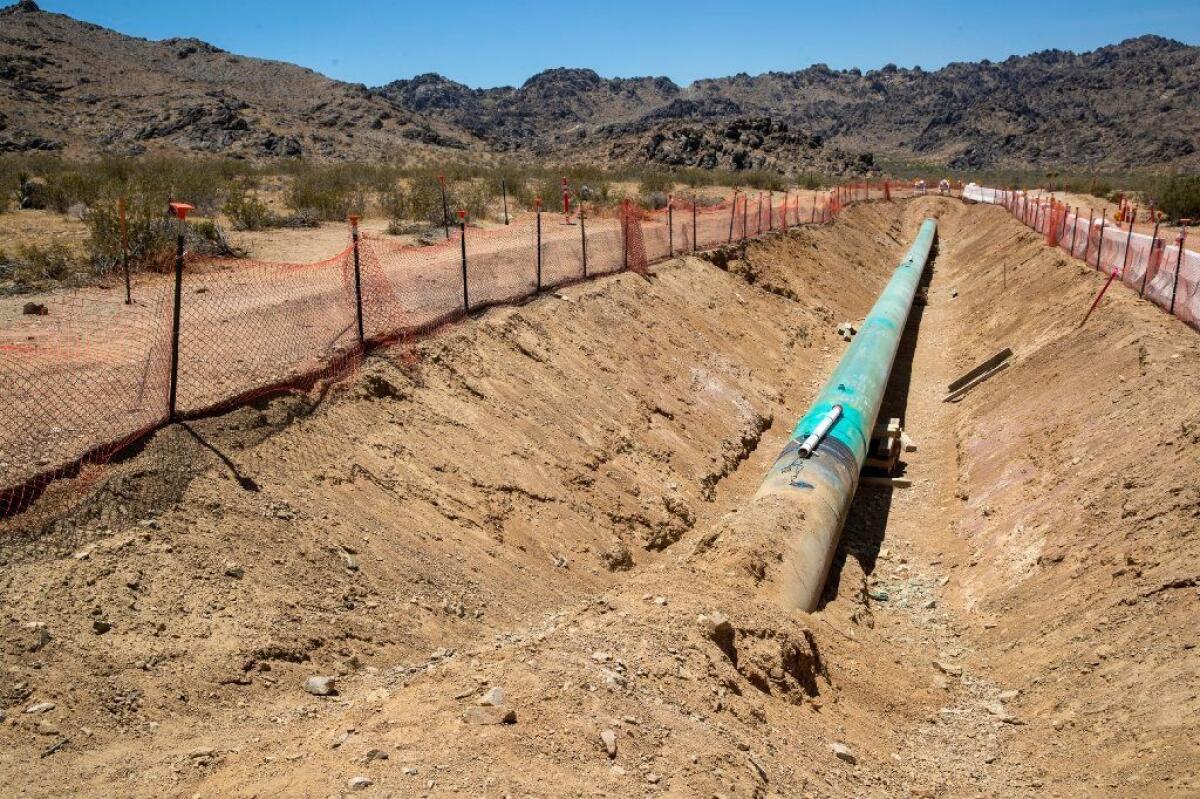 A green gas pipeline in a dirt trench lines by plastic fencing