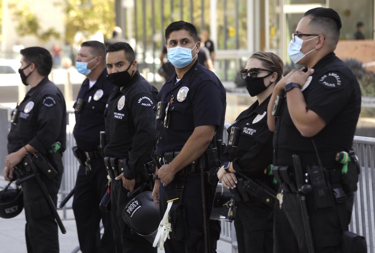 Half a dozen masked Los Angeles Police Department officers stand in front of a barrier.