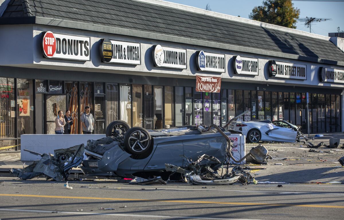 A mangled car upside down in the street surrounded by debris, and a Corvette missing its front end in a parking lot behind