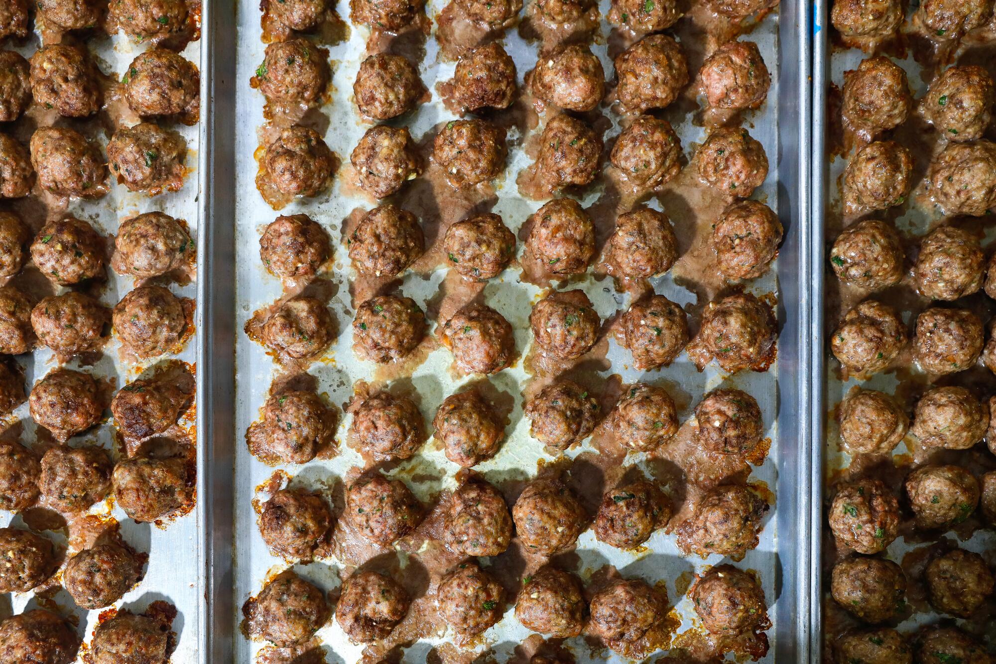 Meatballs fresh out of the oven line multiple pans.