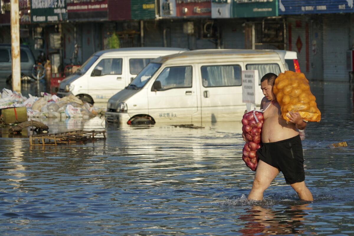 A man carrying sacks of food walks through a street flooded to his knees in China.
