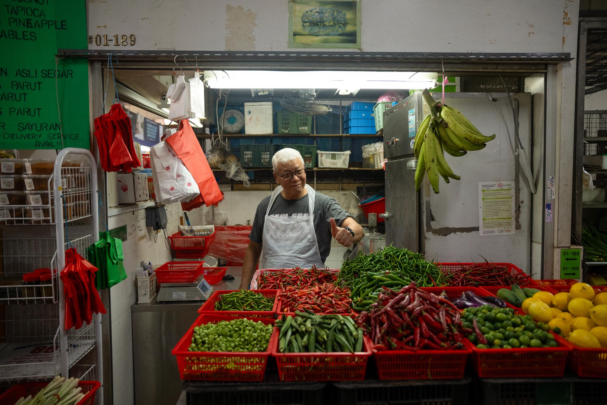 Bir satıcı, Geylang Serai pazarında satılan taze biber, fasulye, bamya, patlıcan ve narenciyeyi beğeniyor.