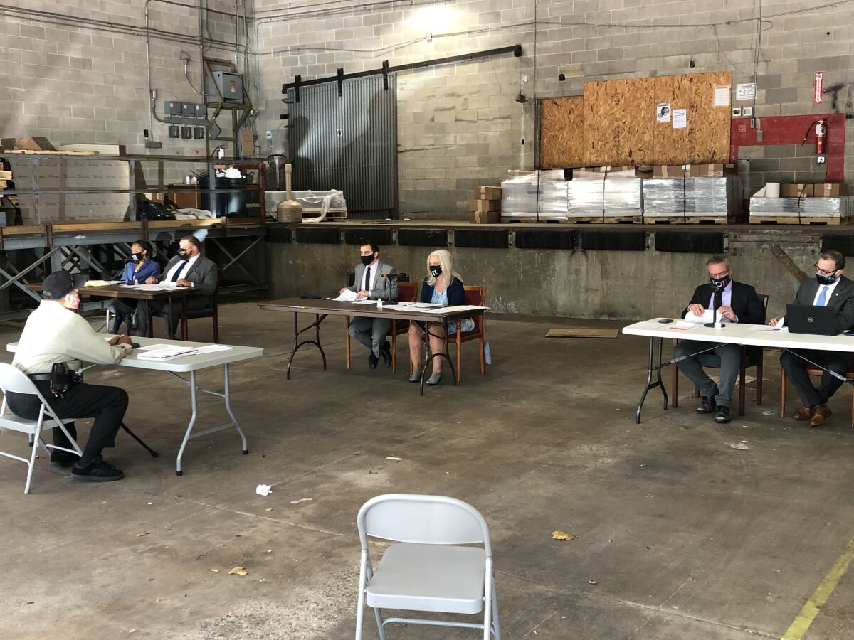 Philadelphia election commission members and others sit at tables during a meeting in an open warehouse.