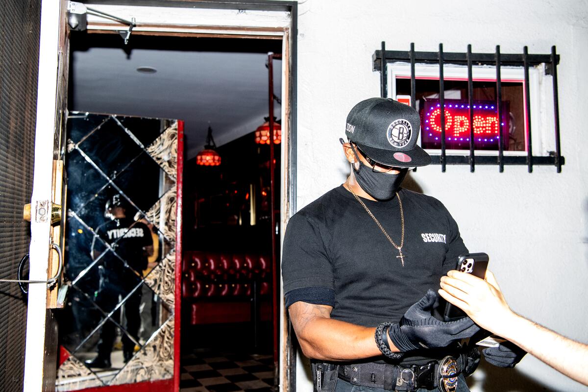 A man in security clothing checks a smartphone held by a customer at the entrance of a bar