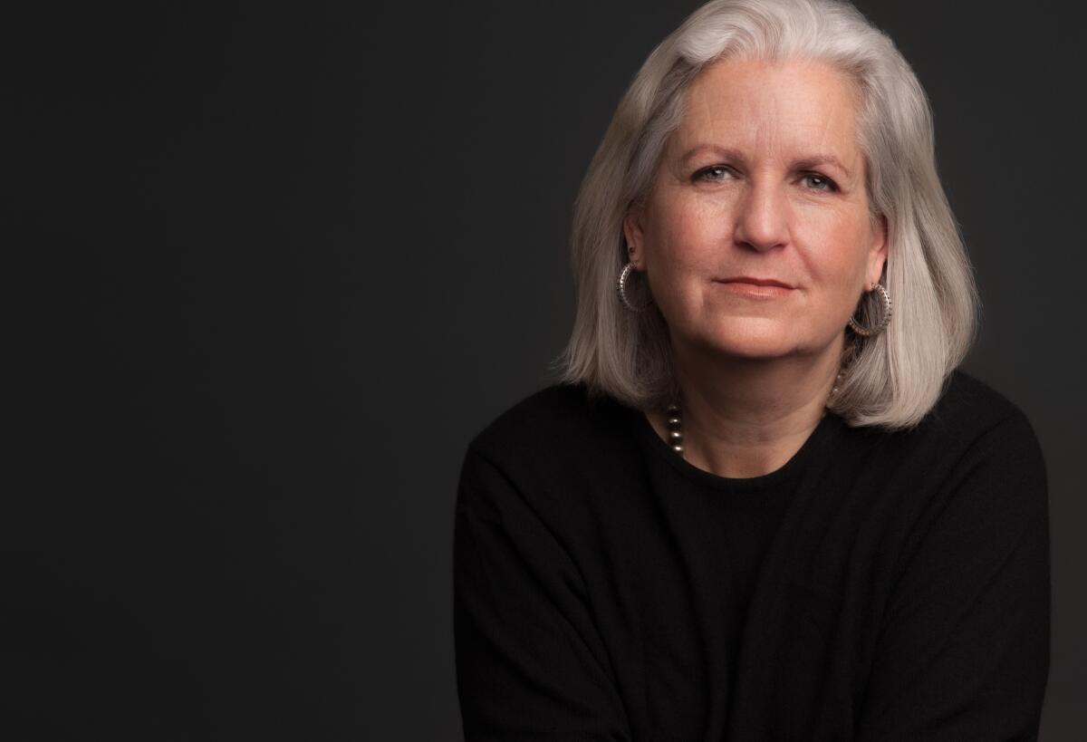 A woman with gray hair sits for a formal portrait against a dark background.