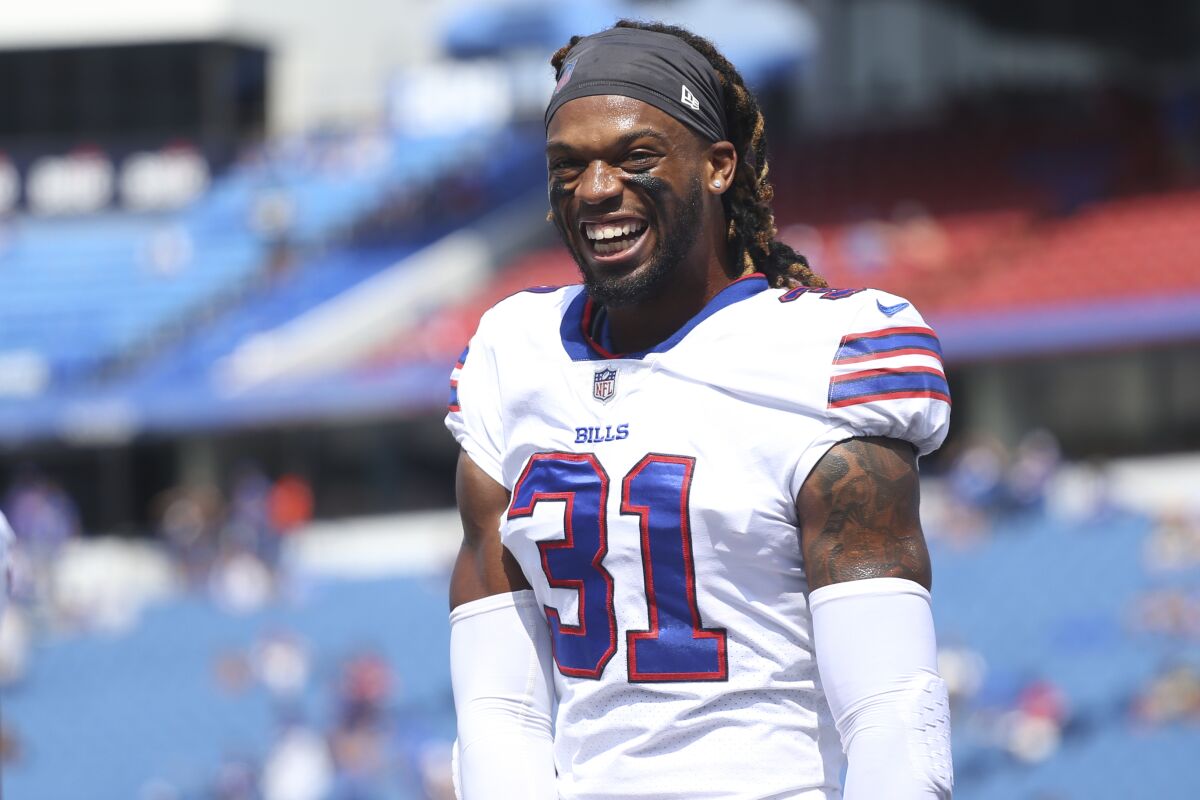 A football player with dreadlocks in a gray headband and white jersey smiles on the field.
