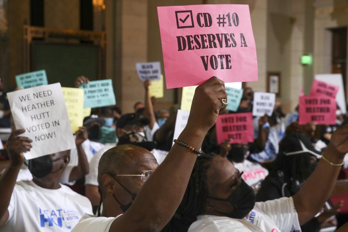 Demonstrators hold signs reading "CD 10 Deserves a Vote" and "We Need Heather Hutt Voted in Now!"