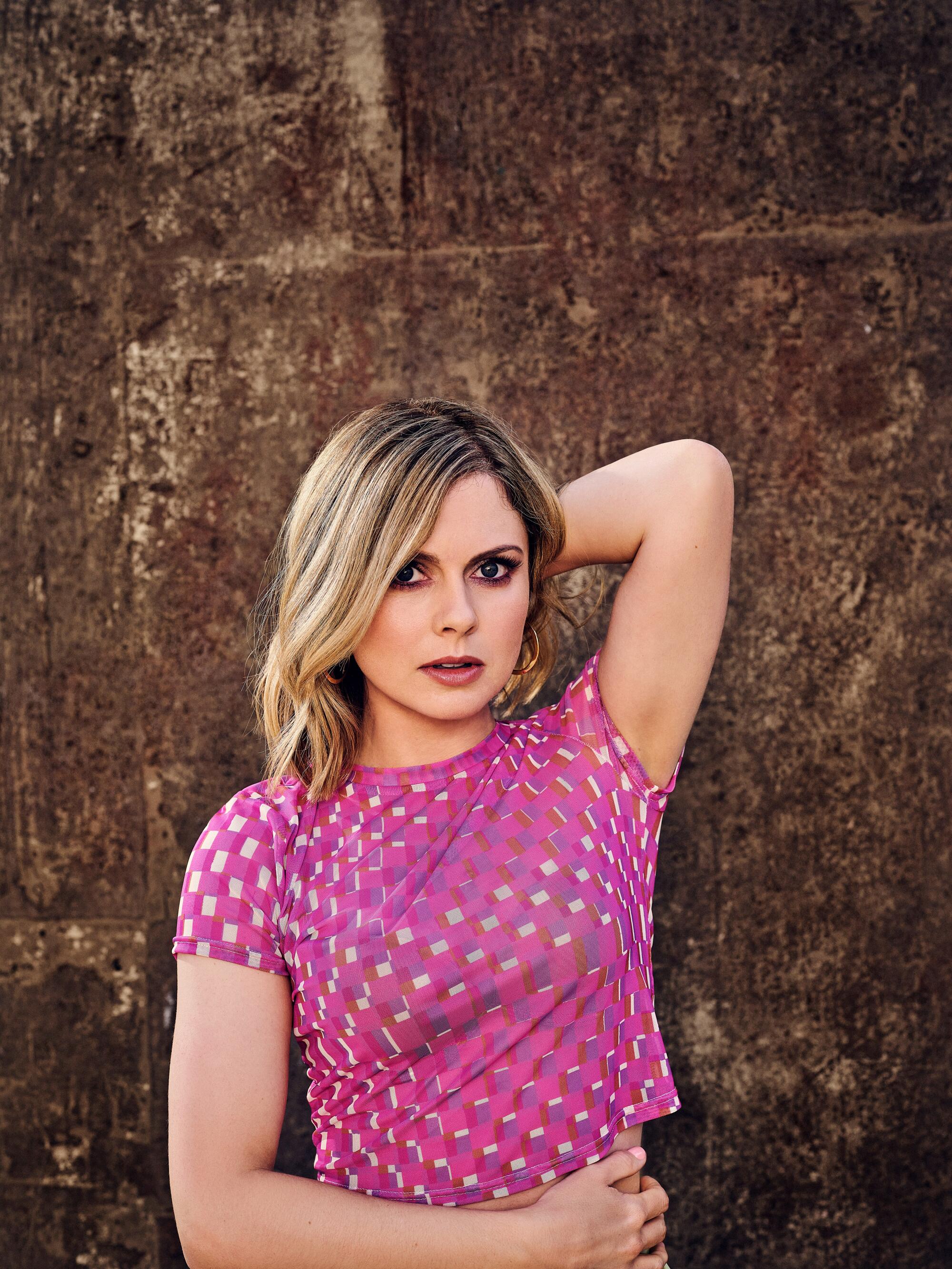 Rose McIver wears a cropped top and covers her midriff with one arm for a portrait.