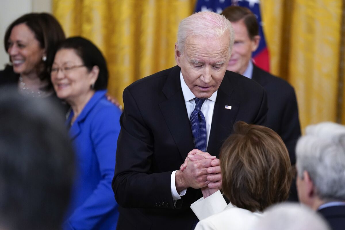 President Biden grasps House Speaker Nancy Pelosi's hand amid a group people at the White House