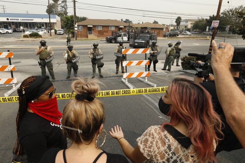 A line of sheriff's deputies with riot shields behind yellow police tape with protesters on the other side