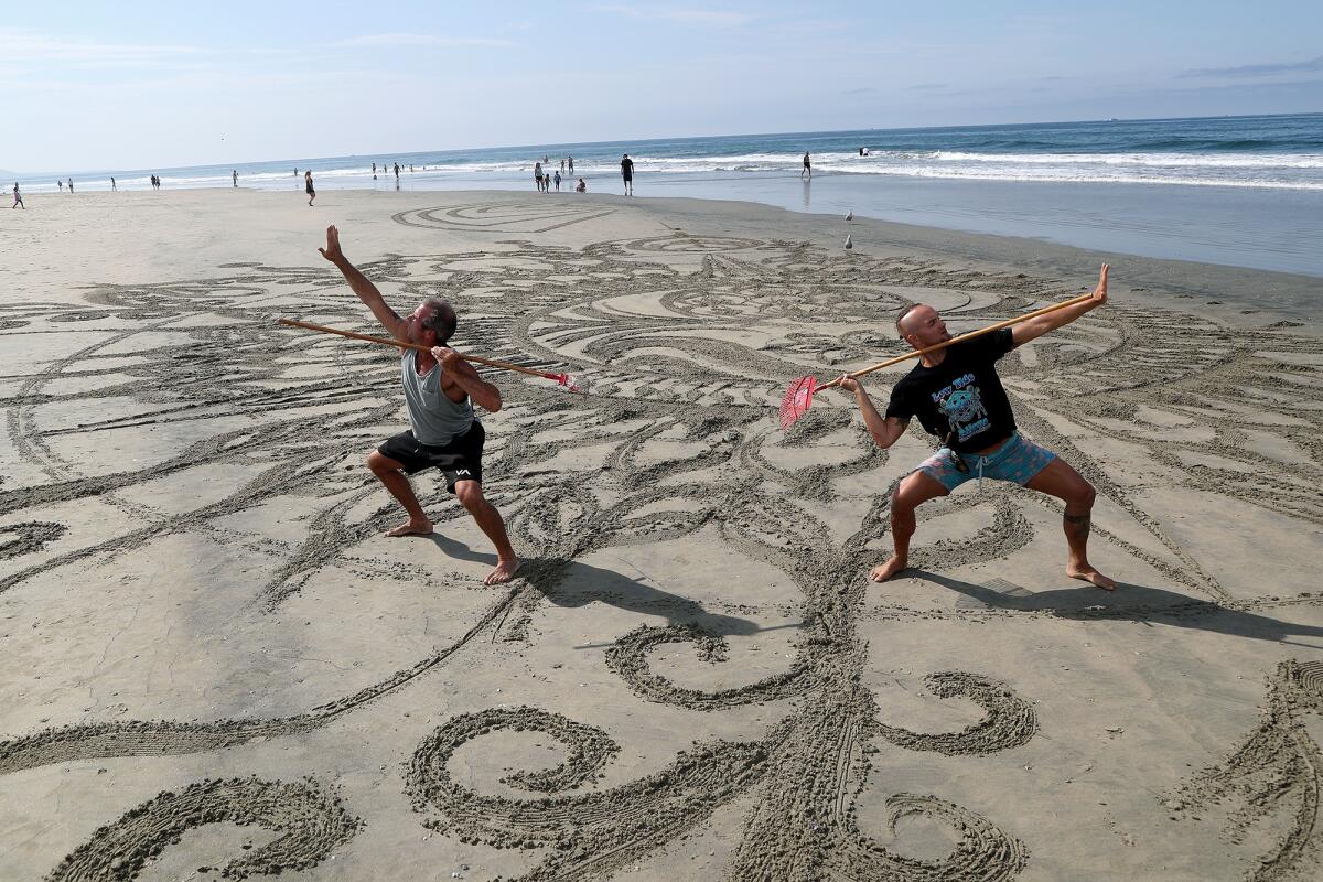 Shane Kern and Drew Davis stand in a warrior pose by their artwork near Newport Beach Pier.