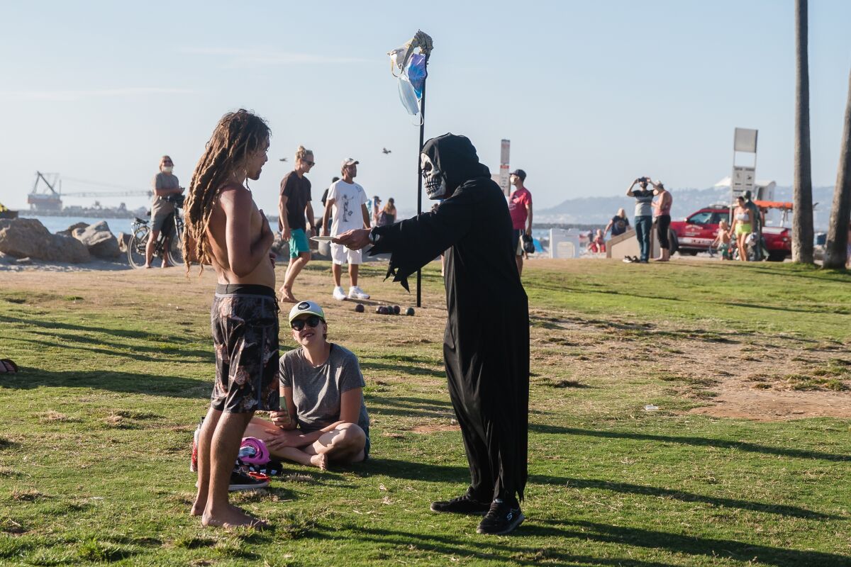 A man dressed as the Grim Reaper tries to give a man a face mask in Ocean Beach on Aug. 12.