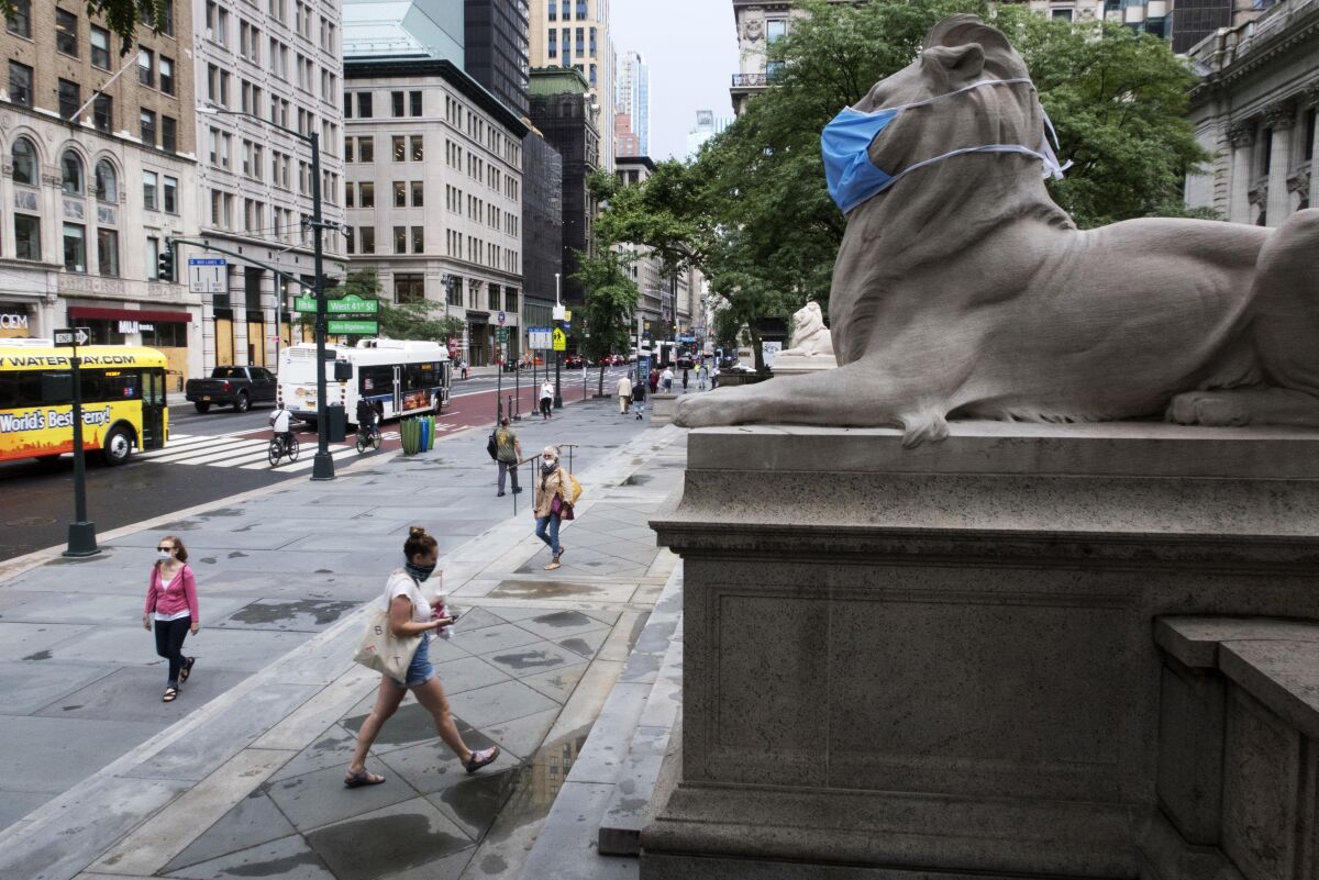 FILE - In this July 1, 2020, file photo, a face mask covers the mouth and nose of one of the iconic lion statues in front of the New York Public Library Main Branch in New York. New York City's public libraries will no longer charge late fees and will waive existing fines for overdue books and other materials, city officials announced Tuesday, Oct. 5, 2021. (AP Photo/Ted Shaffrey, File)