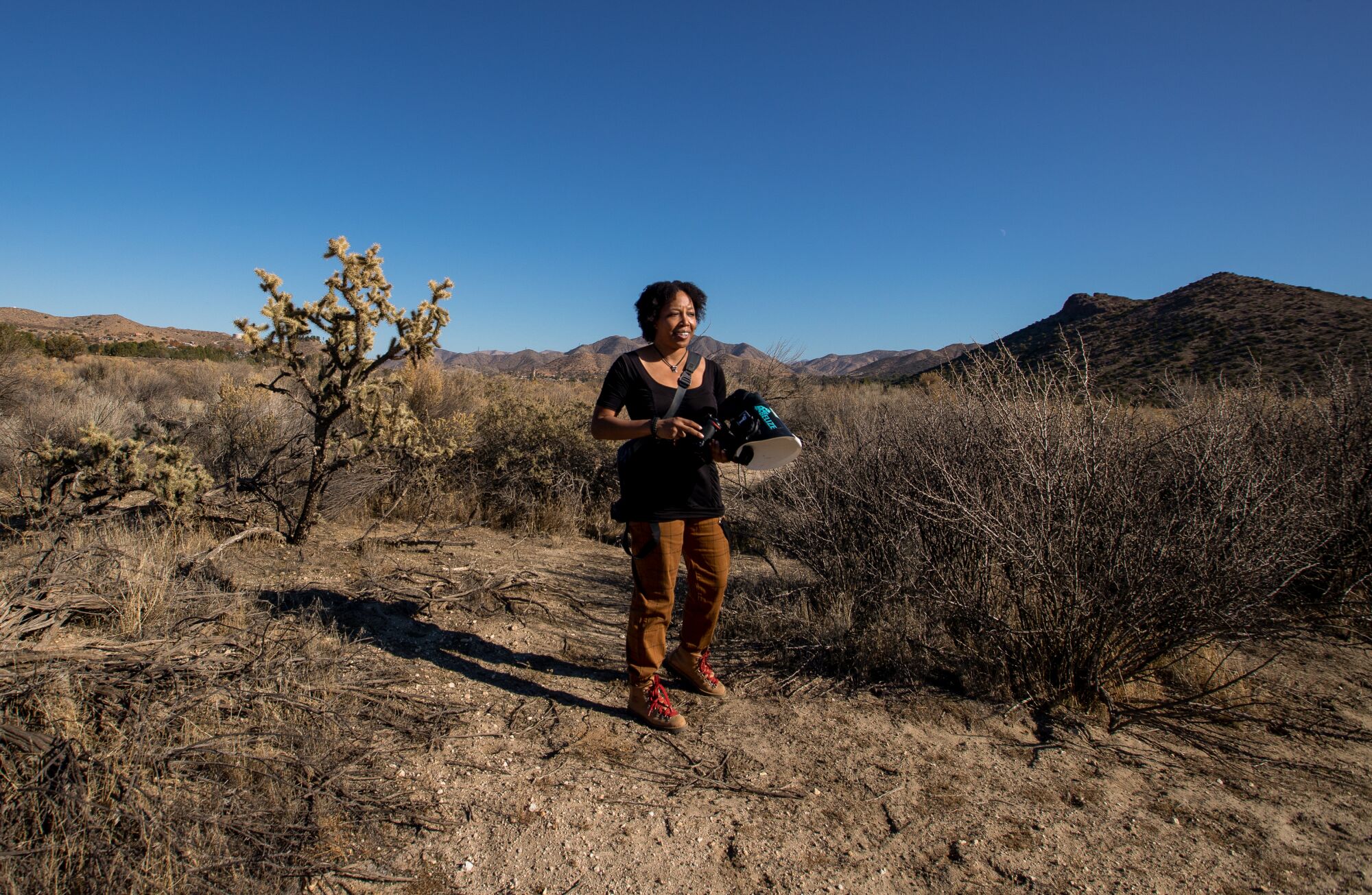 Krystle Hickman standing amid desert chaparral with her camera.