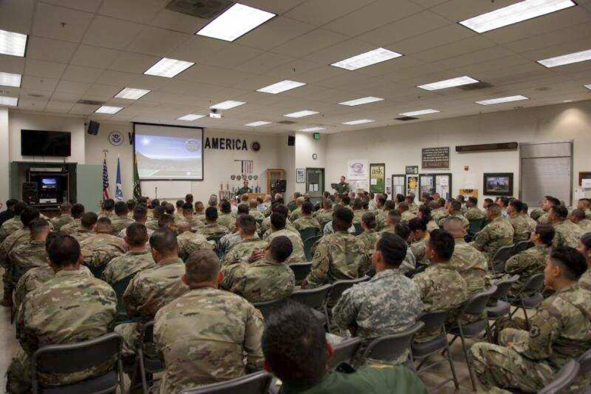 A room full of National Guardsmen are seated in a room in folding chairs