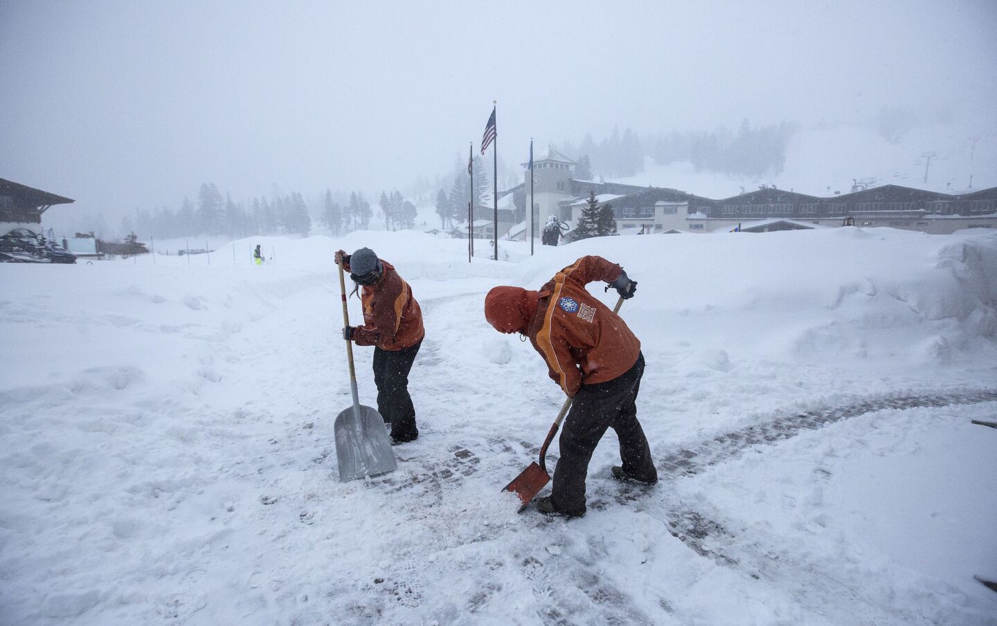 Mammoth Mountain employees clear paths as snow falls lightly Saturday morning.