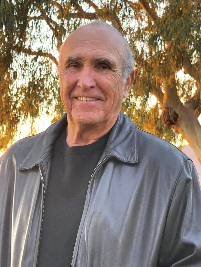 A man in a black T-shirt and leather jacket stands with eucalyptus trees glowing in the setting sun behind him.