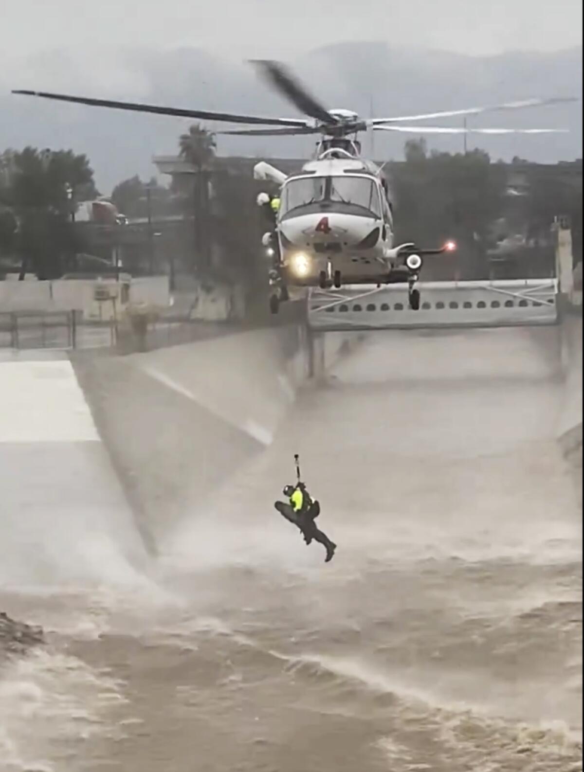 A person dangles from a helicopter over choppy waters within the concrete walls of a manmade river.