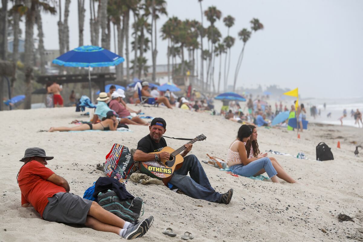 A man plays an acoustic guitar on a crowded beach with palm trees