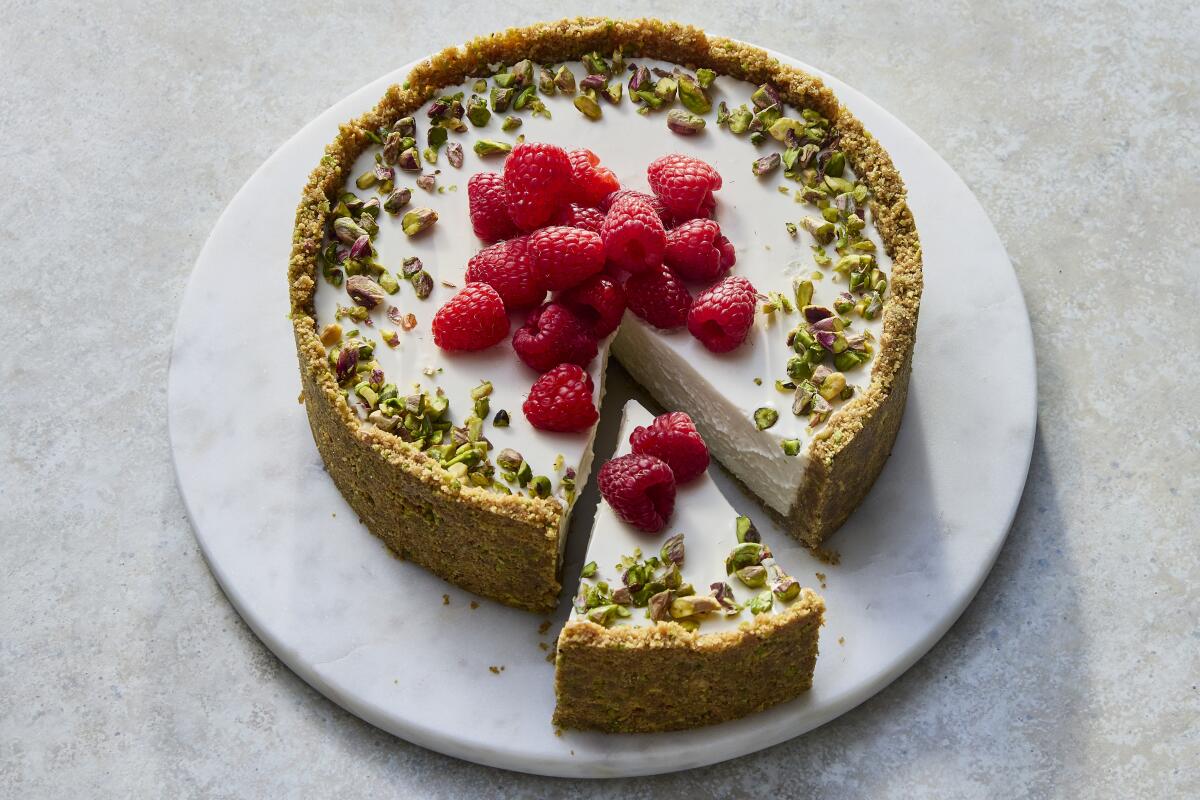 A no-bake cheesecake with chopped pistachios and raspberries on top, and a slice cut out for serving.