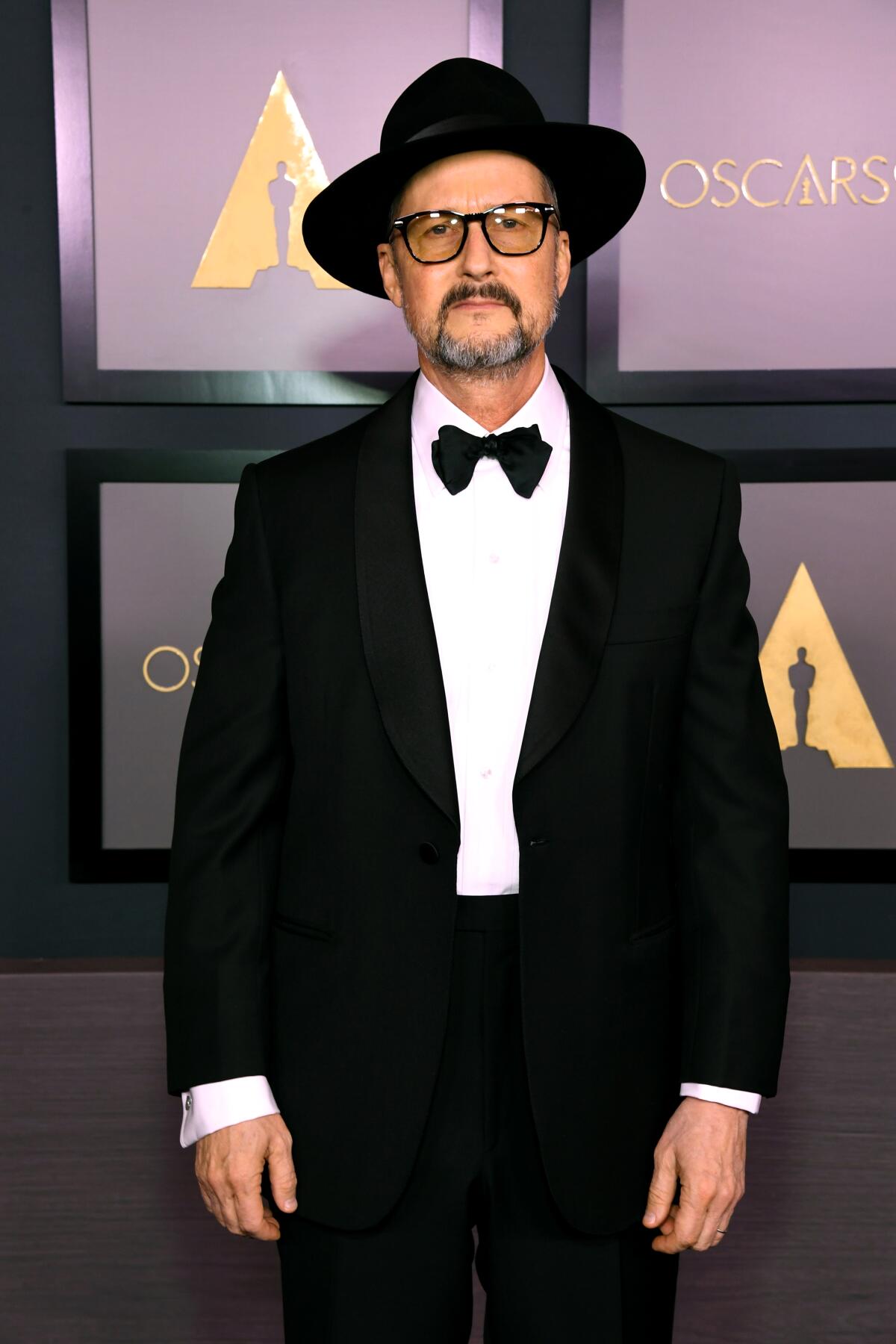 A man in a tux in front of an Oscars backdrop 