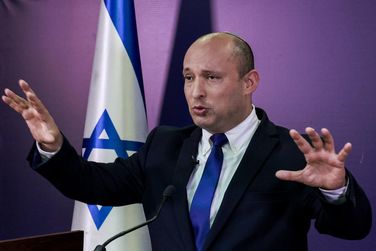 Naftali Bennett gestures in front of an Israeli flag.