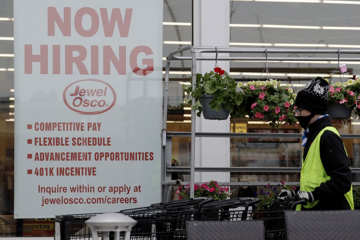 A man pushes carts next to a "now hiring" sign at a grocery store in Deerfield, Ill.