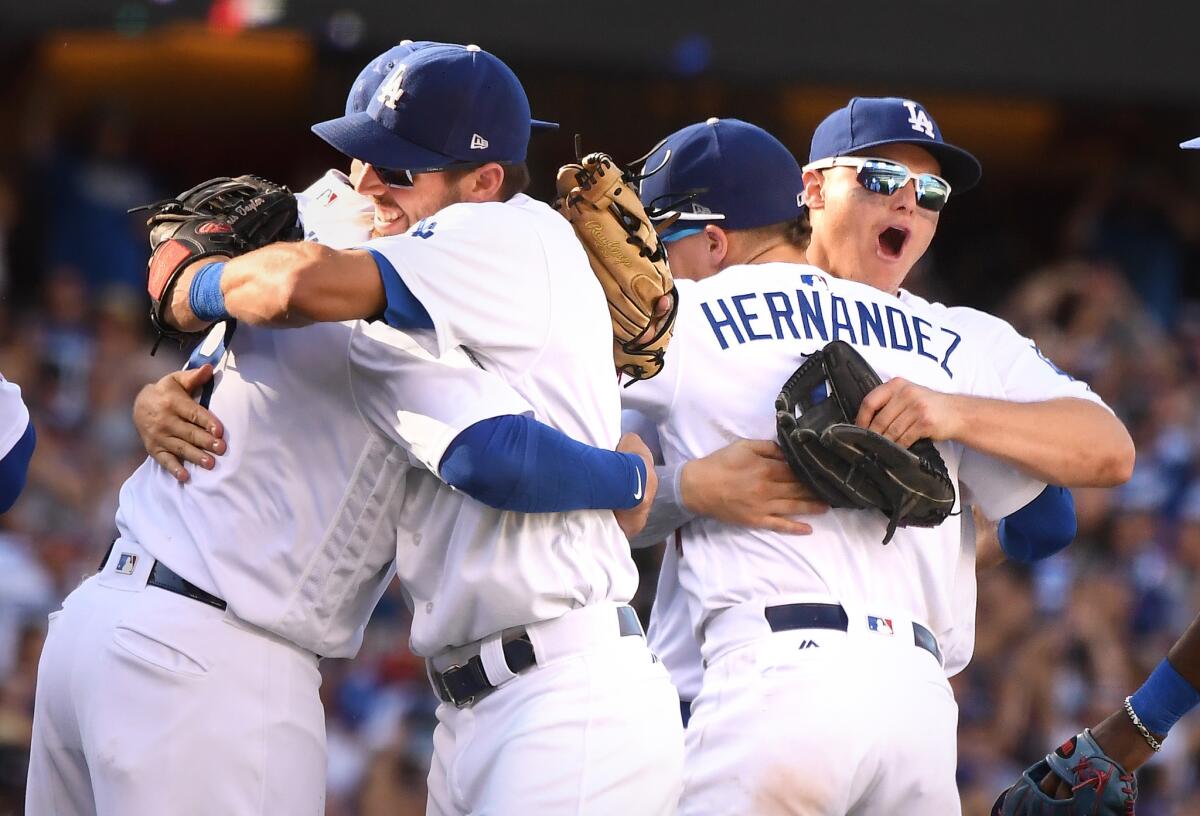 Dodgers shortstop Manny Machado, left, hugs Chris Taylor as Enrique Hernandez and Joc Pederson embrace after defeating the Rockies to win the NL West at Dodger Stadium.