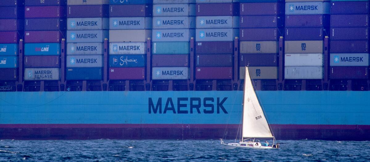 A sailboat against a huge container ship.