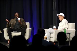 Draymond Green and Trae Young sit on chairs on stage and laugh while taping a podcast