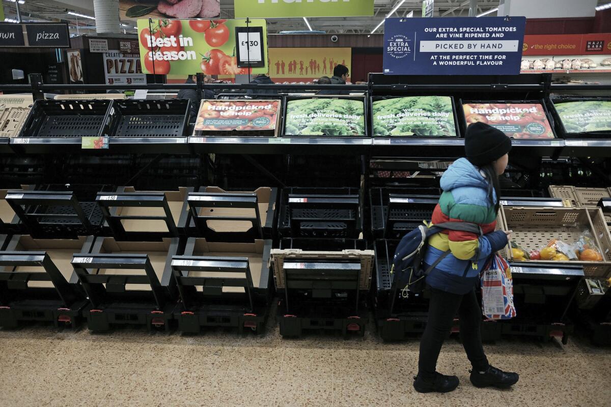 Una niña camina frente a estantes vacíos de la sección de frutas y verduras de un supermercado