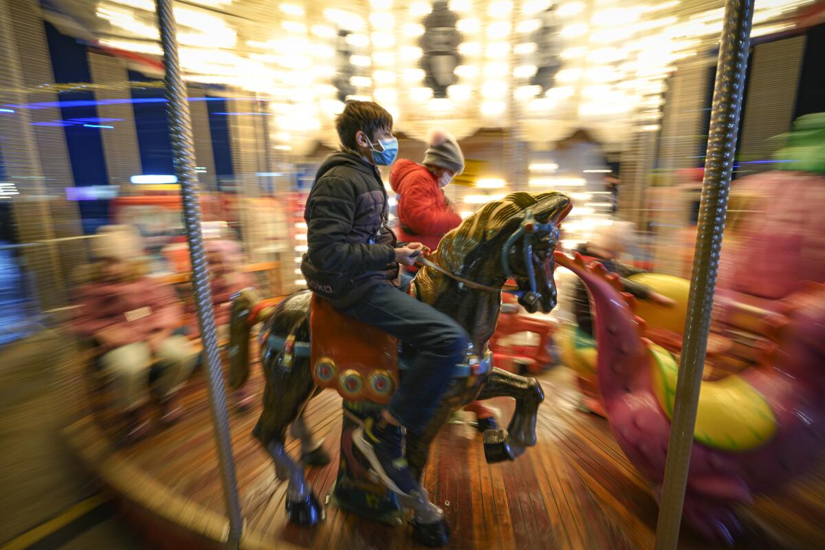 Children, some wearing face masks, enjoy a carousel ride at a Christmas fair in Bucharest, Romania, Saturday, Nov. 27, 2021. The Romanian capital will have three Christmas fairs open for public in the coming weeks and access to the venues will be conditioned by a COVID-19 green pas, proving the holder's vaccination or recovery after the infection. (AP Photo/Vadim Ghirda)