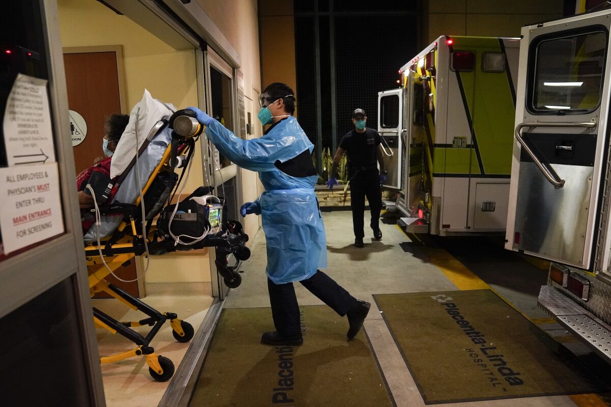 Emergency medical technician Thomas Hoang, 29, of Emergency Ambulance Service, pushes a gurney into an emergency room to drop off a COVID-19 patient in Placentia, Calif., Friday, Jan. 8, 2021. Emergency health workers in California say they're waiting hours to transfer patients from ambulances to hospital emergency rooms due to chronic delays worsened by the nearly two-year coronavirus pandemic. During a state legislative hearing, first responders on Wednesday, Jan. 19, 2022 said taking more than 20 minutes to receive a patient at a hospital emergency room isn’t good for the patient and impedes their ability to head out on new emergency calls. (AP Photo/Jae C. Hong, File)