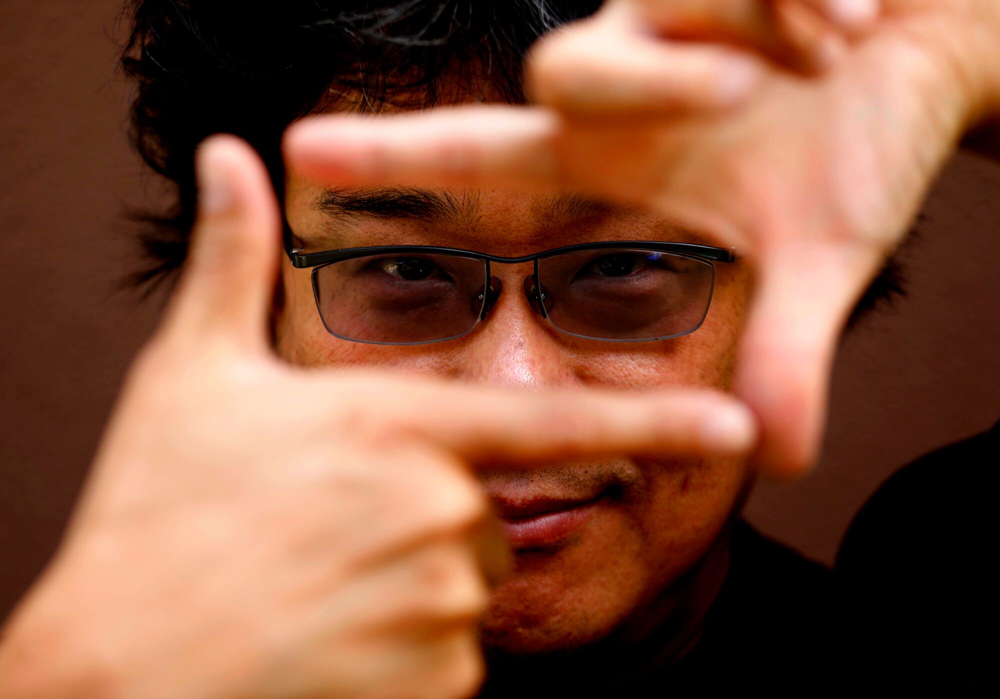 A man uses his hands to create a frame in front of his face.