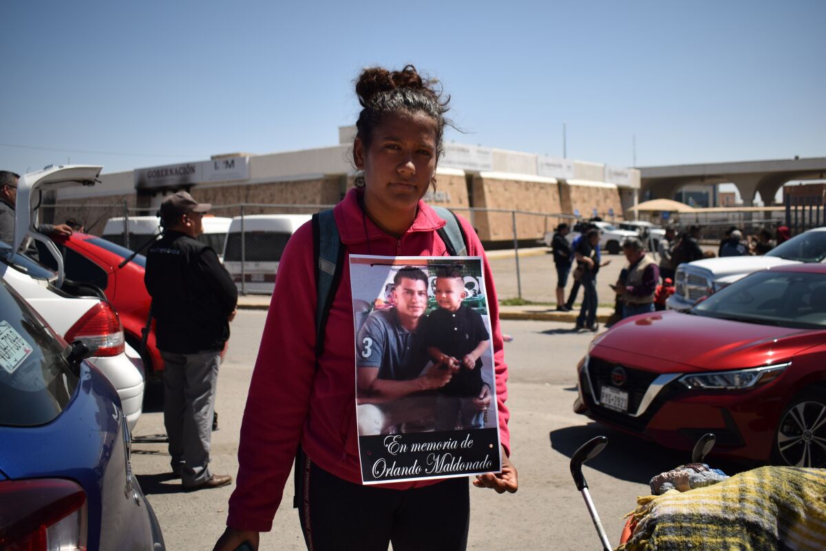 A woman stands outside a building with a poster on her chest with a photo of Orlando Jose Maldonado Perez. 