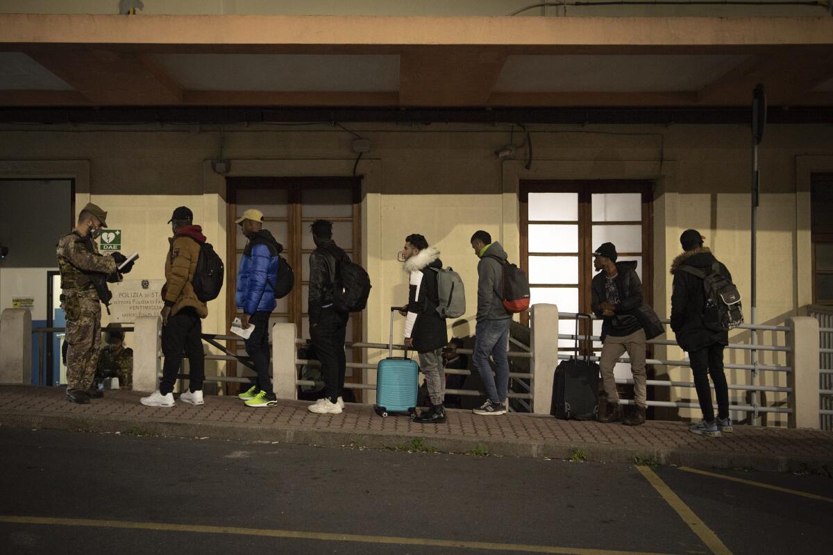 People with backpacks and other luggage lined up on a sidewalk